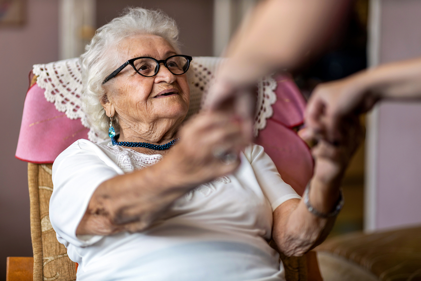 Support for dementia: Elderly lady sat in chair smiling and holding hands with carer